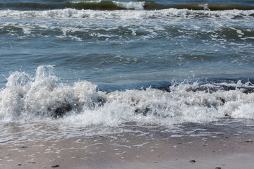 Landscape of beach covered in stones. Blue water. Cloudy sky background.