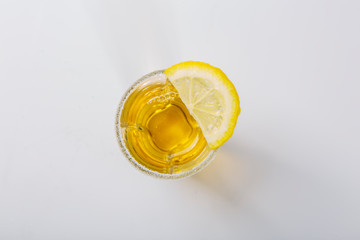 A glass of tequila with lemon stands on a white background. Sprinkle the edge of the glass with...