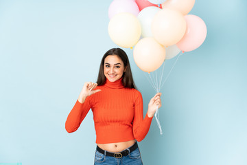 Fototapeta na wymiar Young woman catching many balloons isolated on blue background proud and self-satisfied