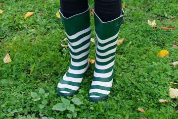 Person wearing clean, green rubber rain boots with white stripes standing in green grass.