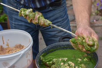 Man putting raw pork on skewer shashlik. Green sauce, marinate.