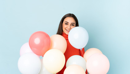 Fototapeta na wymiar Young woman catching many balloons isolated on blue background