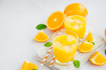 Freshly squeezed orange juice with ice in a glass with a straw on a wooden board on a light background with fresh oranges. Horizontal orientation, copy space.