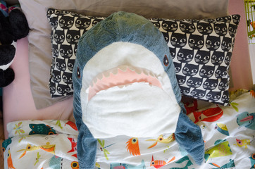 a plushy soft toy shark sleeps in a baby bed covered with a quilt, a baby toy and fun in the kid's room