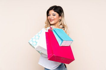 Obraz premium Teenager girl isolated on beige background holding shopping bags and smiling