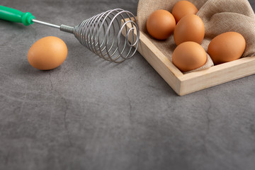 Chicken eggs and egg beater in the wooden tray on the black cement floor. High angle view.