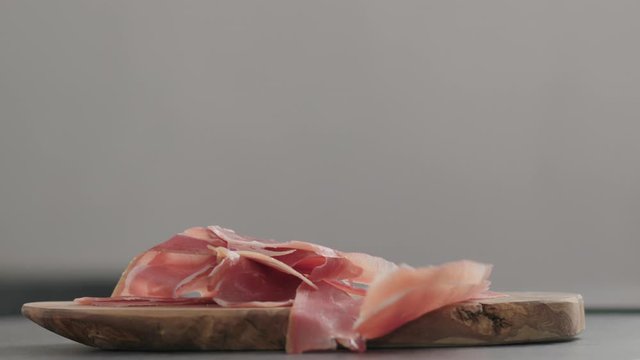 Slow motion prosciutto slices falling on olive wood board