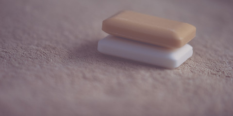 Two bars of soapwhite andorange on a brown towel.