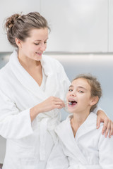 Young woman teaches her little daughter how to brush teeth with toothbrush