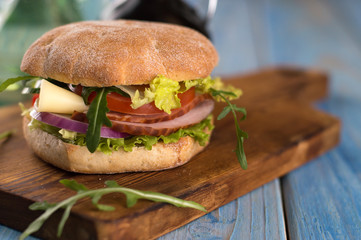 hamburger with vegetables, meat and cheese on a wooden board.