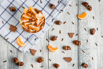 pieces of tangerines in a white cup on a light towel and the wooden background. Chocolate, cloves, acorns