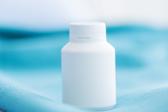 A white medicine bottle on the green bed sheet.