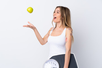 Young woman over isolated white background with weighing machine and with an apple