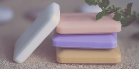 Stack of soap bars different colors on a brown towel with mint plant.
