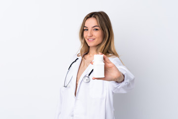 Young woman over isolated white background wearing a doctor gown and holding pills