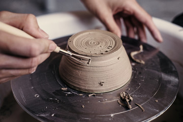 Female potter hands working with clay in workshop. White desk on background