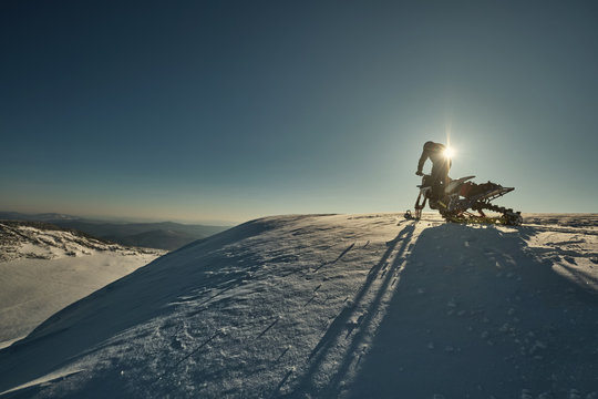 Snowbike rider in mountain valley. Modify dirt bike with snow splashes and trail. Snowmobile sport riding, winter sunny day