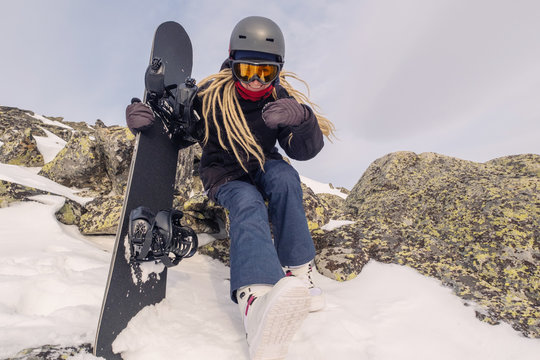 Snowboarder female standing on mountain top, holding the board, going to ride on snow slop