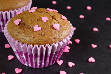 Chocolate muffin decorated with pink sugar hearts. Black background. Close-up