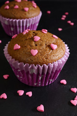 Chocolate muffin decorated with pink sugar hearts. Black background. Close-up