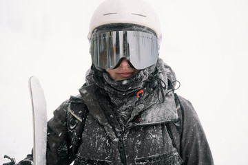 Portrait of snowboarder with board wearing mask in snowy winter landscape outdoors