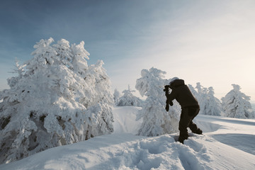 Photographer female snowboarder taking a photos of beautiful winter landscape on sunset