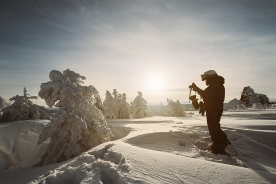 Photographer female snowboarder taking a photos of beautiful winter landscape on sunset