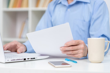 Senior man reads document and works on laptop in the office