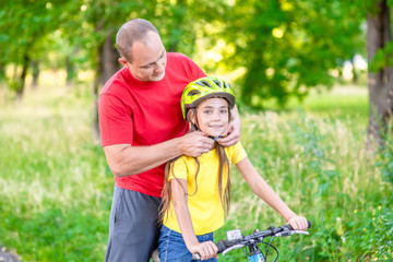 Happy family. Father fastens his daughter a bicycle helmet