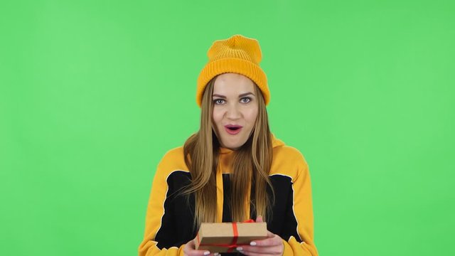 Portrait of modern girl in yellow hat is opening the gift, very surprised and upset. Green screen