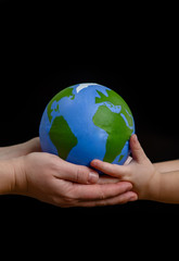 Close up hands of mother gives the planet into the hands of a child. Isolated on dark background