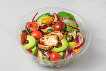 Healthy chicken salad with avocado, tomatoes and pomegranate in plastic package for take away or food delivery