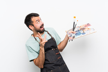 Young artist man holding a palette over isolated background nervous and scared