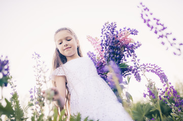 Naklejka premium Cute girl with long hair in a white dress picks flowers.