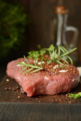 Fresh raw piece of beef steak with herbs and spices on wooden board on a dark background. A good piece of meat for cooking dinner.