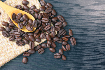 Coffee beans are scattered in wooden spoons and on sack bags and wooden patterned background