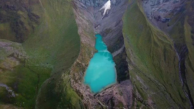 Aerial, reverse, drone shot high above the emerald glacier lake, Laguna Humantay, in Andes mountains, overcast, in Cusco region, Peru