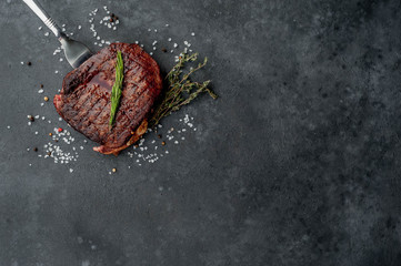 Beef steak on a fork on a stone background with spices with copy space for your text.