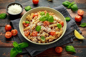Healthy Chicken, fusilli pasta with tomatoes, basil and parmesan cheese. on wooden table.