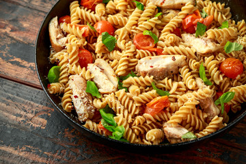 Healthy Chicken, fusilli pasta with tomatoes, basil and parmesan cheese in iron pan.