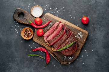 Grilled beef steak on a cutting board with spices and tomatoes on a stone background