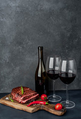 Dinner for two. Beef steak on a cutting board with spices and a bottle of wine with  glasses on stone background