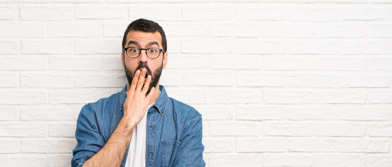 Handsome man with beard over white brick wall surprised and shocked while looking right
