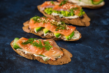 healthy sandwiches with smoked salmon avocado cucumber cream cheese on rye bread on dark blue background