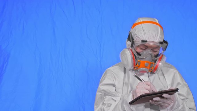 Scientist virologist in respirator makes write in an tablet computer with stylus. Woman wearing protective medical mask. Concept health safety virus coronavirus epidemic 2019 nCoV. Chroma key blue.