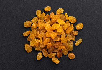Pile of dried yellow raisins on black background