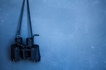 Binoculars infocus in the background of a dark blue wall