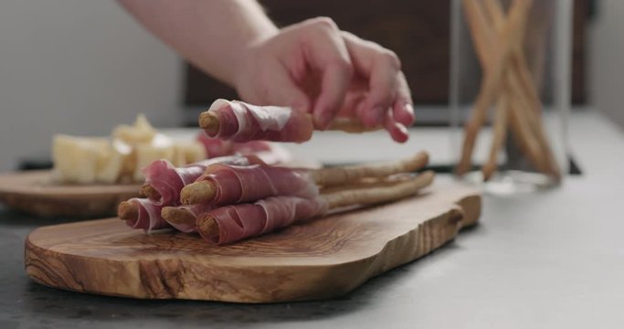 Slow motion man hand take grissini with prosciutto from olive board