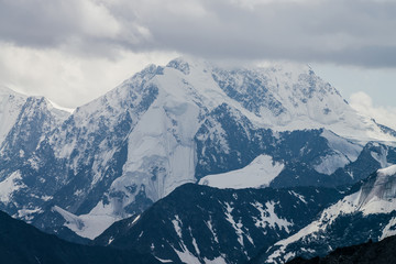 Awesome landscape with huge glacial mountains in bad cloudy weather. Low stormy clouds touch top of snowy mountain with glaciers. Storm is coming due to mountains. Gloomy overcast atmospheric scenery.