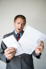 Shocked businessman opening his mail with an open mouth gasp of surprise